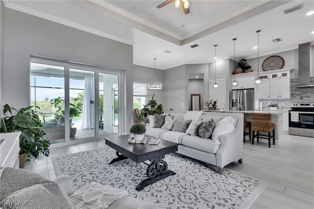 living room featuring ornamental molding, ceiling fan with notable chandelier, and light hardwood / wood-style flooring