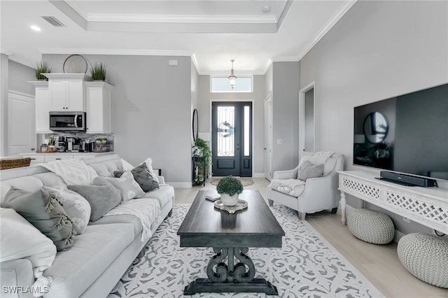 living room featuring ornamental molding, light wood-type flooring, and a tray ceiling