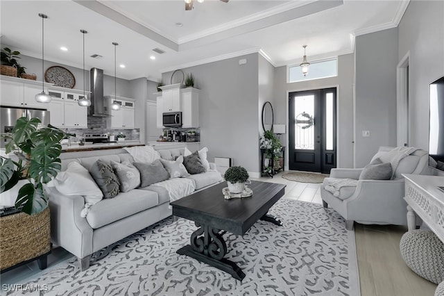 living room with ornamental molding, light hardwood / wood-style floors, and a raised ceiling