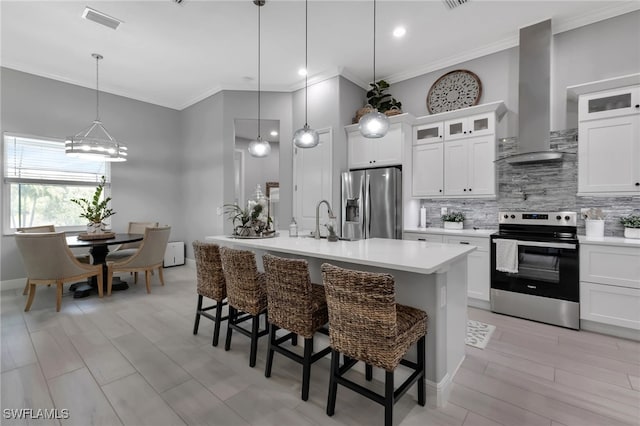 kitchen featuring wall chimney range hood, hanging light fixtures, stainless steel appliances, an island with sink, and a kitchen bar