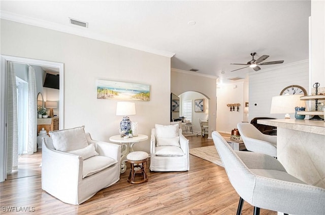 sitting room with arched walkways, visible vents, ornamental molding, a ceiling fan, and light wood-type flooring