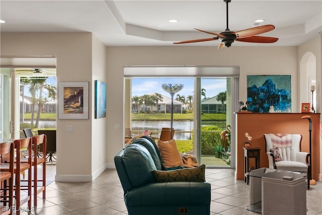 living room featuring light tile patterned floors, a raised ceiling, ceiling fan, and a water view