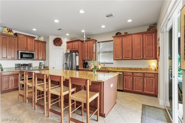 kitchen featuring a kitchen breakfast bar, a center island, light tile patterned floors, light stone counters, and stainless steel appliances