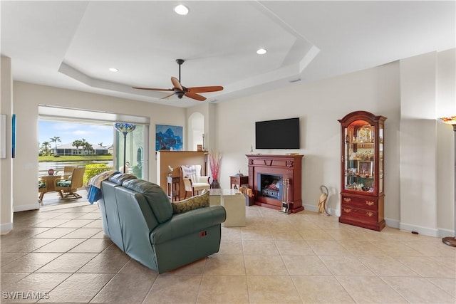 living room with light tile patterned flooring, ceiling fan, and a tray ceiling