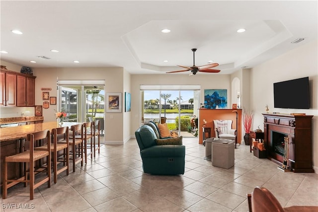 tiled living room featuring a raised ceiling, ceiling fan, and a fireplace