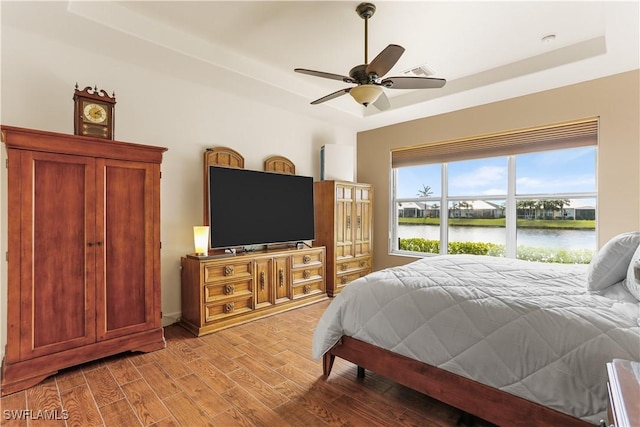 bedroom featuring ceiling fan, a raised ceiling, and light hardwood / wood-style floors