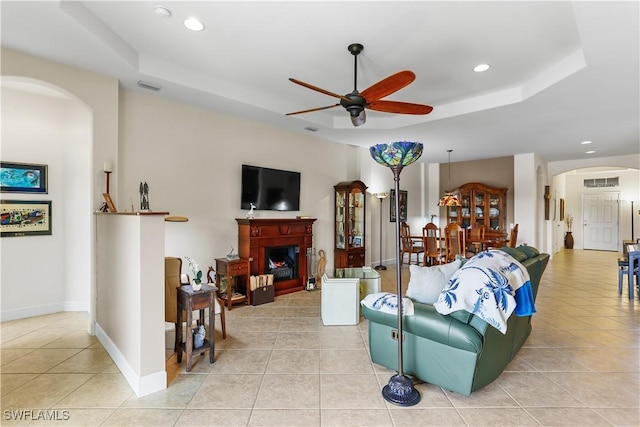 living room with a tray ceiling, ceiling fan, and light tile patterned flooring