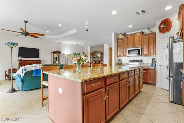 kitchen featuring a kitchen island, a breakfast bar area, light tile patterned floors, stainless steel appliances, and light stone countertops