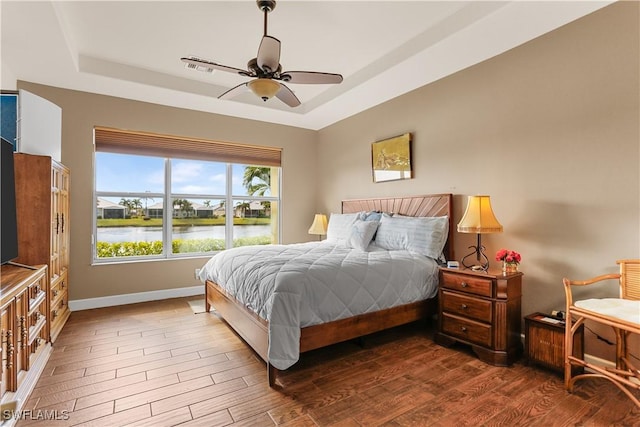 bedroom featuring a water view, hardwood / wood-style floors, ceiling fan, and a tray ceiling