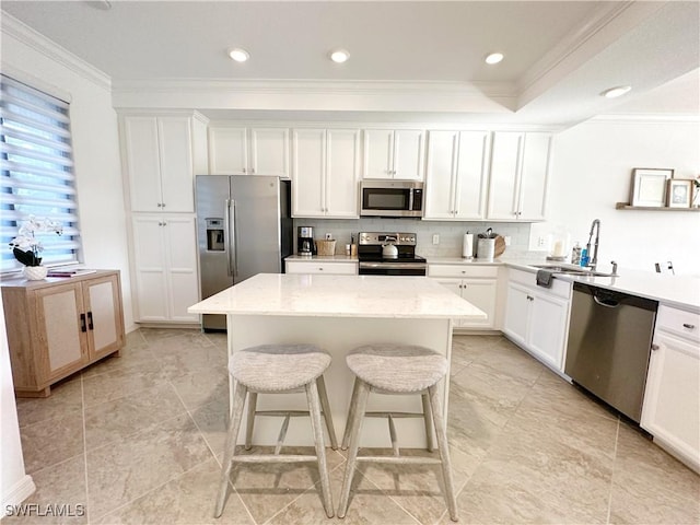 kitchen featuring crown molding, a kitchen island, stainless steel appliances, light stone countertops, and white cabinets