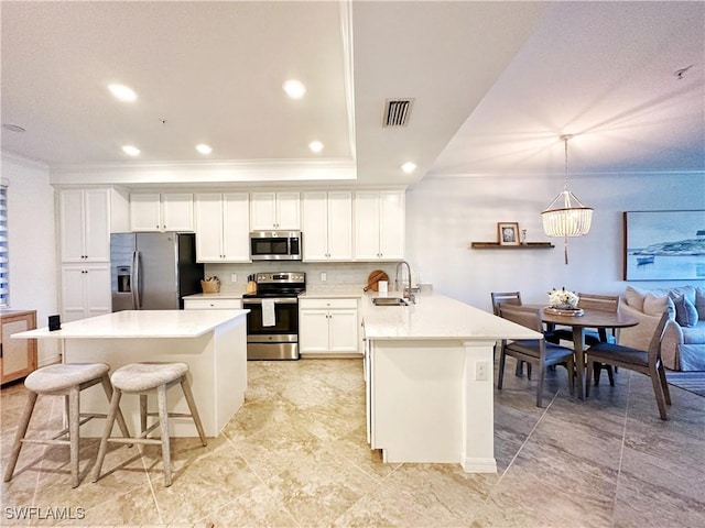 kitchen featuring a kitchen bar, sink, hanging light fixtures, appliances with stainless steel finishes, and white cabinets