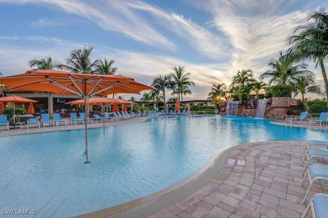 pool at dusk featuring pool water feature and a patio area