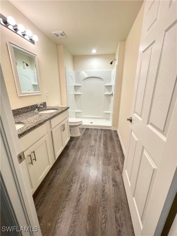 bathroom with hardwood / wood-style flooring, vanity, toilet, and walk in shower