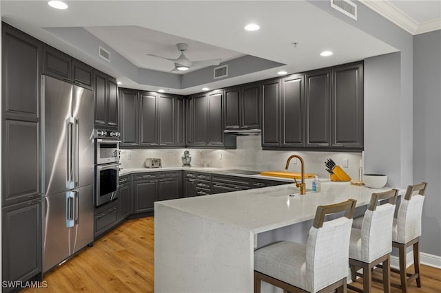 kitchen featuring appliances with stainless steel finishes, sink, a breakfast bar area, kitchen peninsula, and light hardwood / wood-style flooring