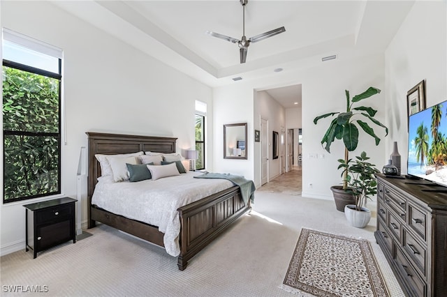 carpeted bedroom featuring multiple windows, a raised ceiling, and ceiling fan