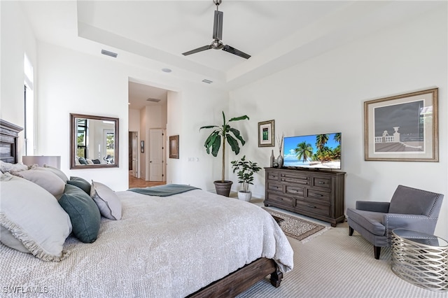 bedroom featuring a tray ceiling, light colored carpet, ceiling fan, and a towering ceiling