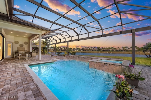 pool at dusk featuring a lanai, a patio, a water view, pool water feature, and an in ground hot tub