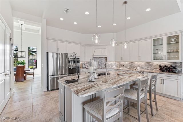 kitchen with a kitchen island with sink, light stone countertops, white cabinetry, and stainless steel appliances