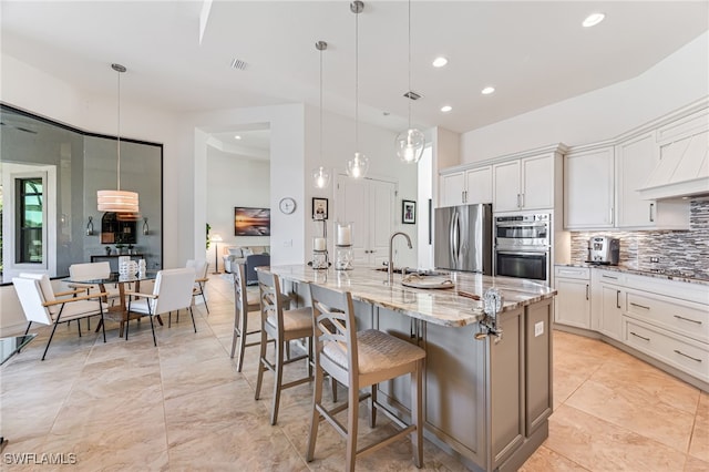 kitchen featuring stainless steel appliances, white cabinetry, a kitchen island with sink, and pendant lighting