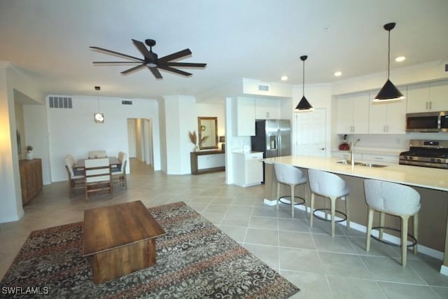 kitchen featuring sink, appliances with stainless steel finishes, hanging light fixtures, white cabinets, and a kitchen bar