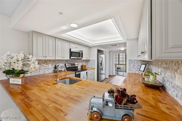 kitchen featuring appliances with stainless steel finishes, butcher block counters, sink, decorative backsplash, and a raised ceiling