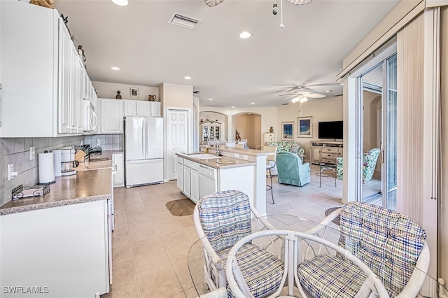 kitchen featuring sink, white appliances, white cabinets, and a center island with sink