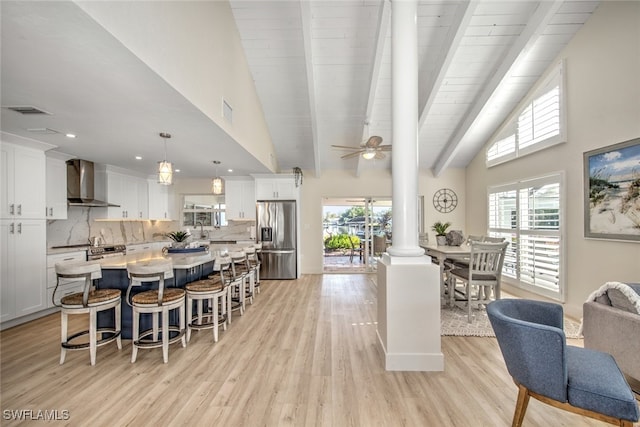 dining room featuring a healthy amount of sunlight, beam ceiling, decorative columns, and light wood-type flooring