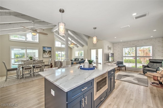 kitchen with pendant lighting, stainless steel microwave, light stone countertops, and a kitchen island