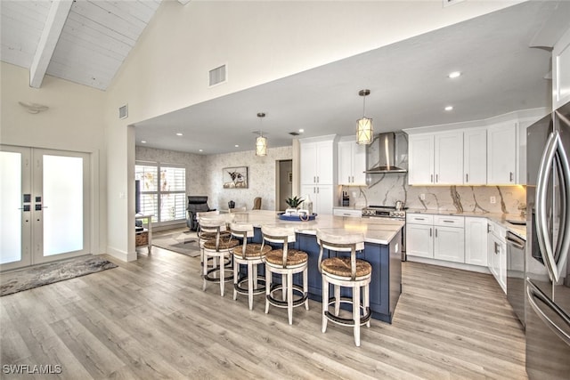 kitchen with wall chimney exhaust hood, decorative light fixtures, a kitchen island, stainless steel appliances, and white cabinets