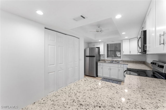 kitchen with appliances with stainless steel finishes, sink, white cabinets, ceiling fan, and a tray ceiling