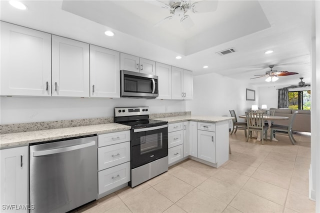 kitchen featuring appliances with stainless steel finishes, a raised ceiling, kitchen peninsula, ceiling fan, and white cabinets