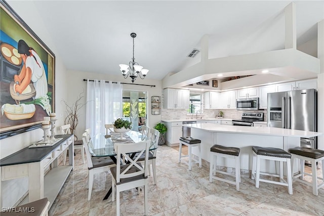 kitchen with appliances with stainless steel finishes, white cabinetry, decorative backsplash, vaulted ceiling, and decorative light fixtures