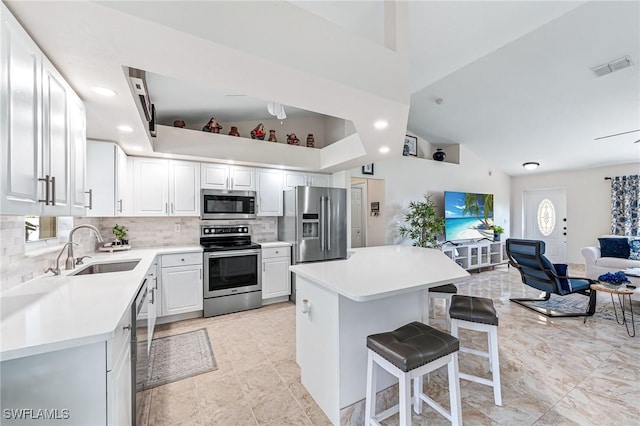 kitchen featuring sink, appliances with stainless steel finishes, a kitchen breakfast bar, tasteful backsplash, and white cabinets