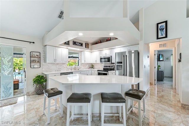 kitchen with sink, a breakfast bar area, appliances with stainless steel finishes, decorative backsplash, and white cabinets