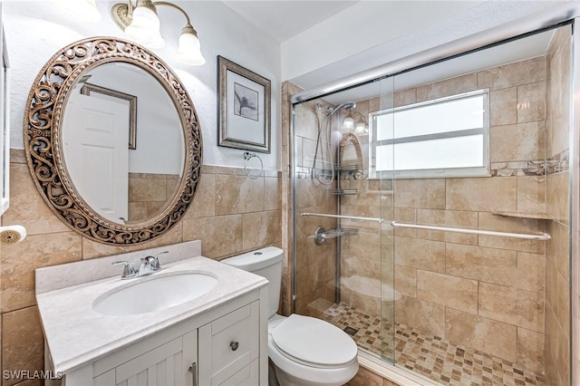 bathroom with walk in shower, vanity, toilet, and tile walls