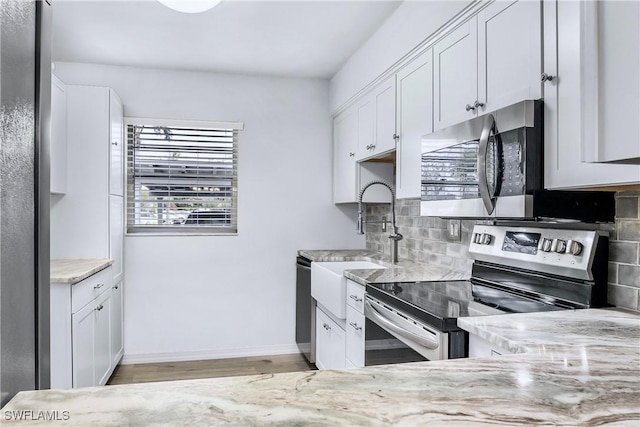 kitchen featuring tasteful backsplash, appliances with stainless steel finishes, white cabinets, light stone countertops, and baseboards