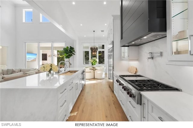 kitchen with stainless steel appliances, wall chimney range hood, light countertops, and white cabinets