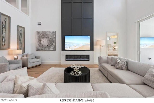 living room with baseboards, visible vents, a glass covered fireplace, a towering ceiling, and wood finished floors