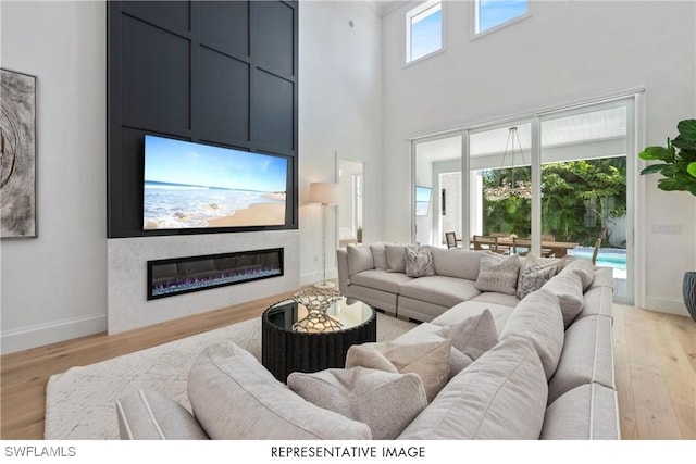 living area featuring a wealth of natural light, a glass covered fireplace, light wood-style floors, and baseboards