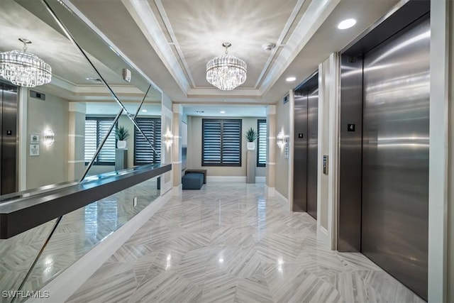 hall featuring a raised ceiling, ornamental molding, elevator, and an inviting chandelier