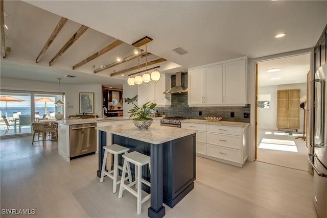 kitchen featuring wall chimney range hood, kitchen peninsula, pendant lighting, stainless steel appliances, and white cabinets