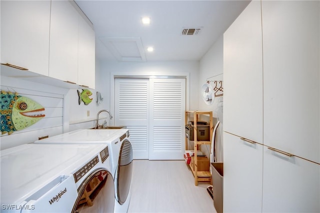 clothes washing area featuring cabinets, sink, washer and dryer, and light hardwood / wood-style flooring