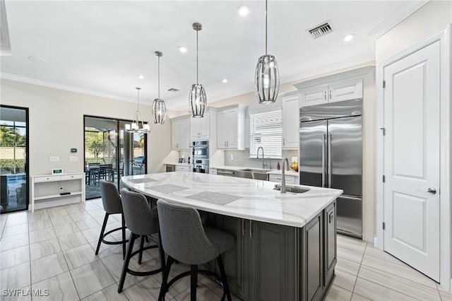 kitchen with an island with sink, pendant lighting, stainless steel appliances, light stone countertops, and white cabinets