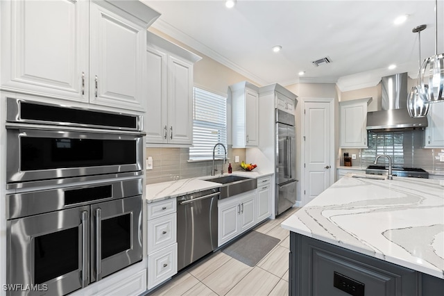 kitchen with pendant lighting, white cabinets, backsplash, stainless steel appliances, and wall chimney exhaust hood