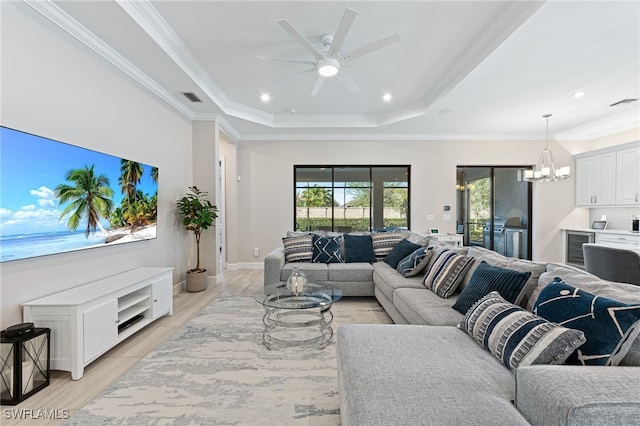 living room with light wood-type flooring, ornamental molding, a raised ceiling, beverage cooler, and ceiling fan with notable chandelier