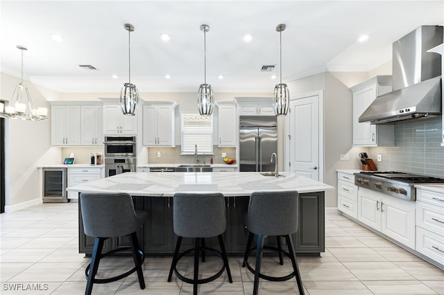 kitchen featuring stainless steel appliances, wall chimney exhaust hood, a large island, and hanging light fixtures