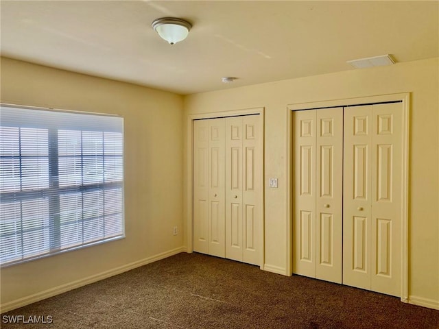 unfurnished bedroom with multiple closets and dark colored carpet