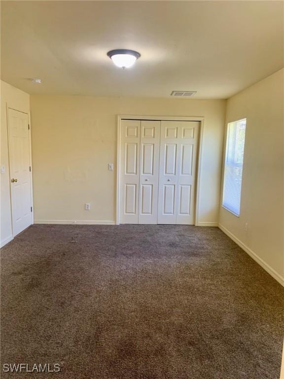 unfurnished bedroom with dark carpet and a closet