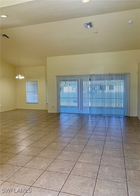 spare room featuring light tile patterned flooring, lofted ceiling, and a notable chandelier