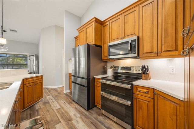 kitchen featuring stainless steel appliances, wood-type flooring, and decorative light fixtures